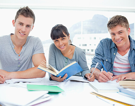 Drei Schüler sitzen an einem Tisch mit Lernunterlagen