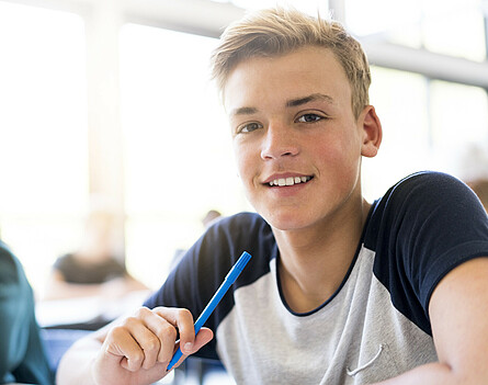 Ein Oberstufenschüler beim Lernen. Er lächelt motiviert in die Kamera