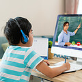 Bub mit Kopfhörern sitzt vorm PC bei Online Unterricht
