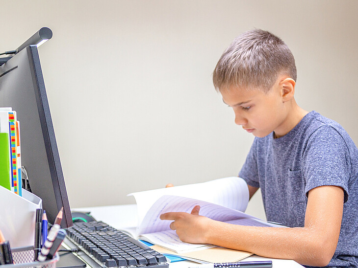 Ein Unterstufenschüler sitzt an seinem Schreibtisch und ist konzentriert mit seinen Schulsachen beschäftigt