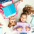 Zwei Volksschülerinnen mit Heften und Stiften am Boden liegend