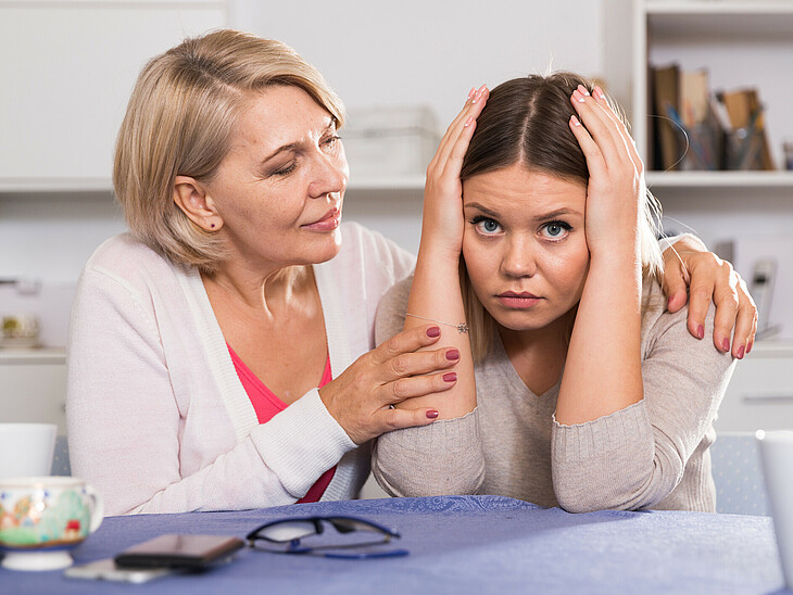 Verzweifelte Tochter wird von Mutter umarmt und unterstützt