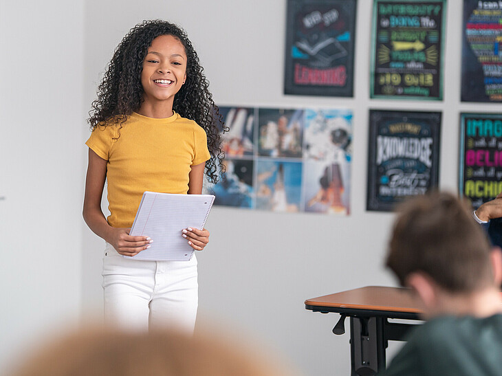 Eine Schülerin steh vor ihren Mitschülern in der Klasse und hält ein Referat