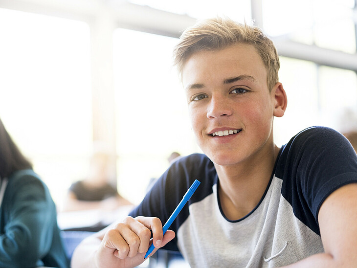 Ein Oberstufenschüler beim Lernen. Er lächelt motiviert in die Kamera