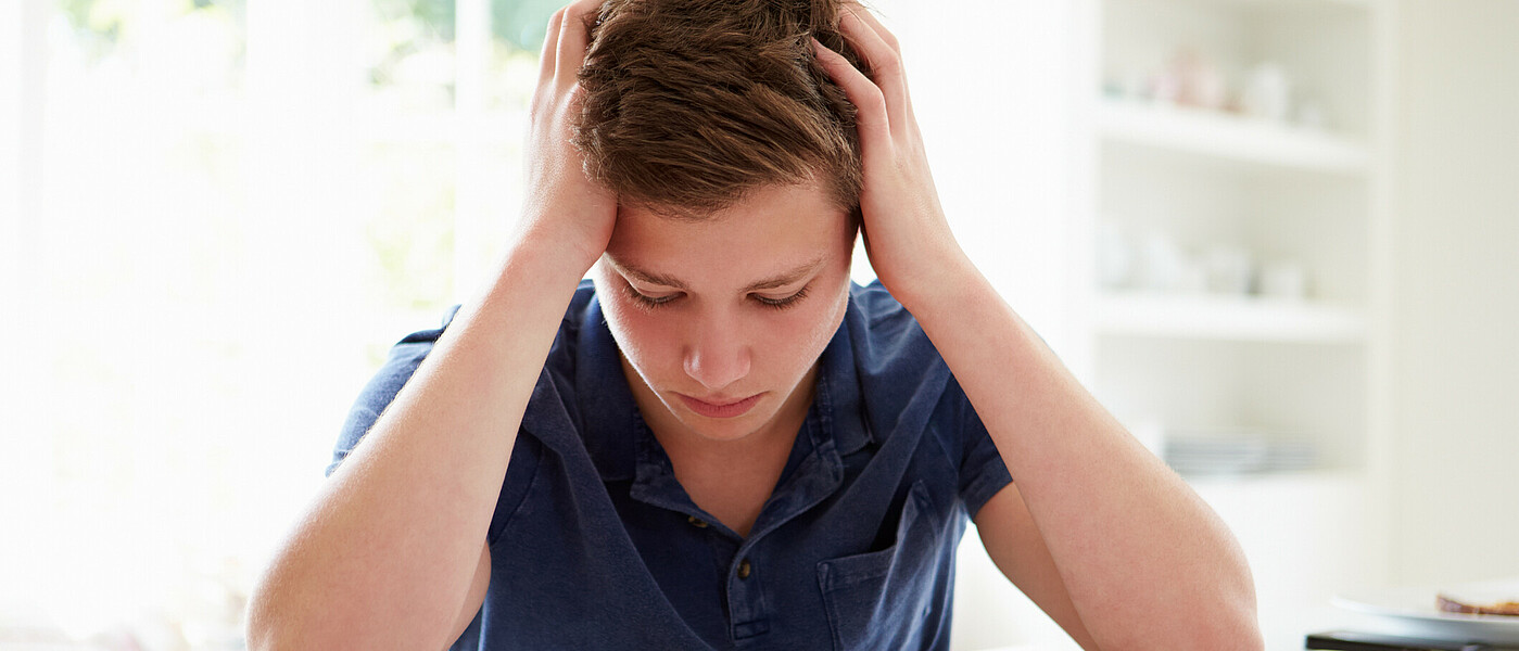 Ein Schüler stützt, über eine Aufgabe gebeugt, seinen Kopf verzweifelt in die Hände