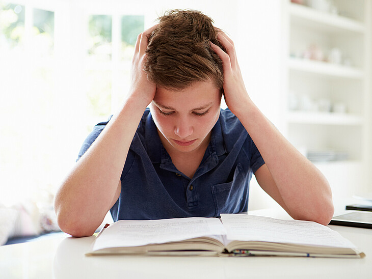 Ein Schüler stützt, über eine Aufgabe gebeugt, seinen Kopf verzweifelt in die Hände