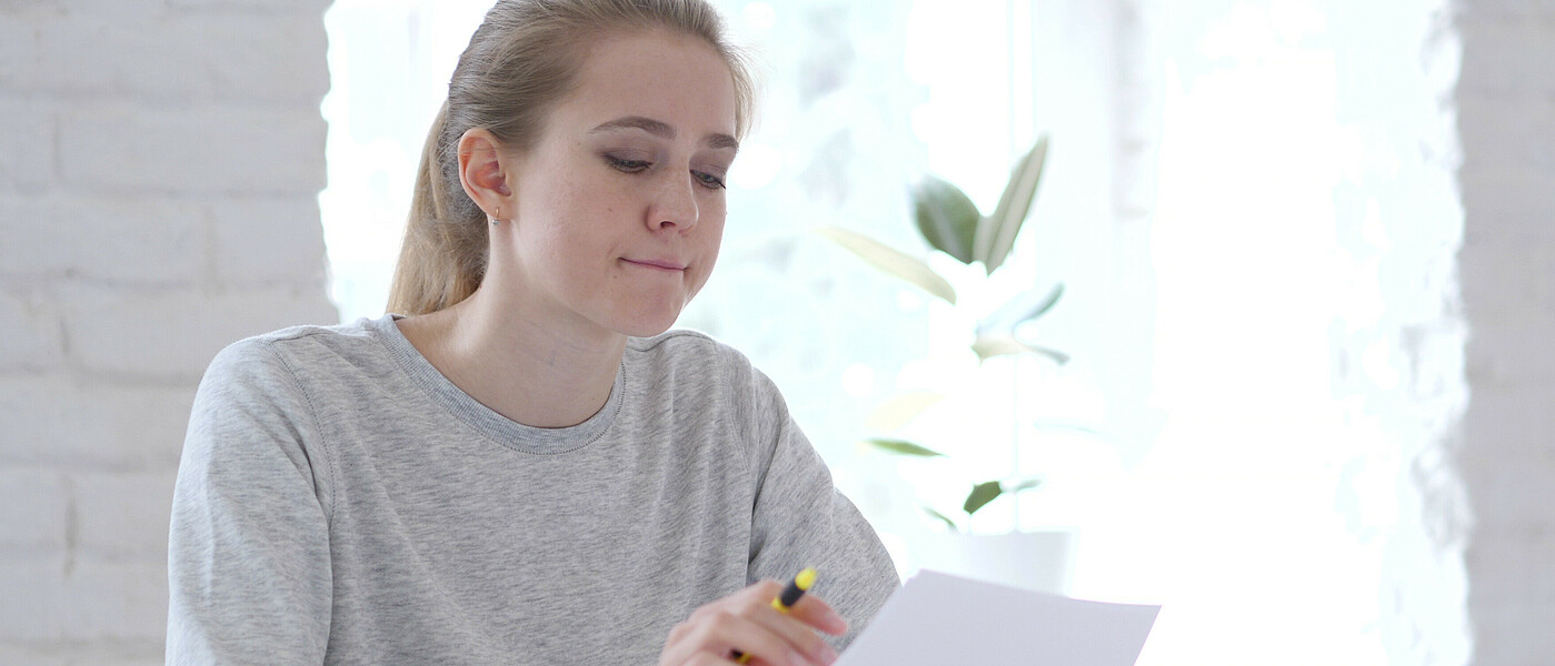 Oberstufenschülerin mit Zettel in der Hand, denkt nach.