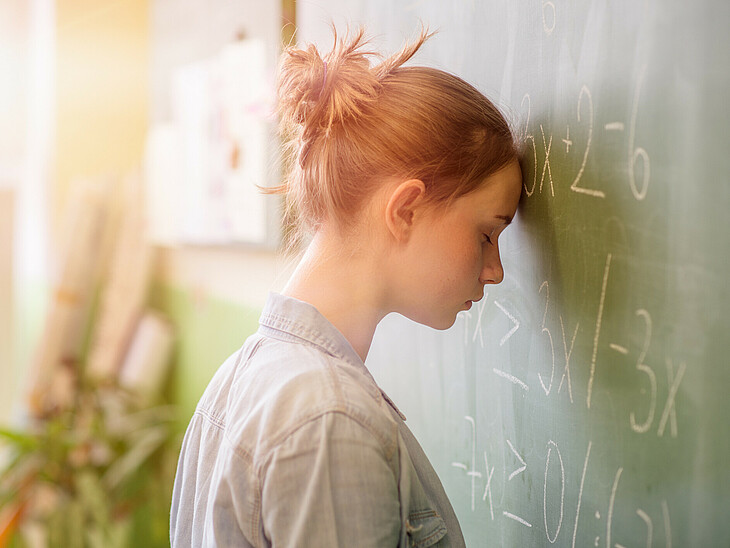 Verzweifelte Schülerin stützt ihre Stirn an der Tafel beim Rechnen ab.