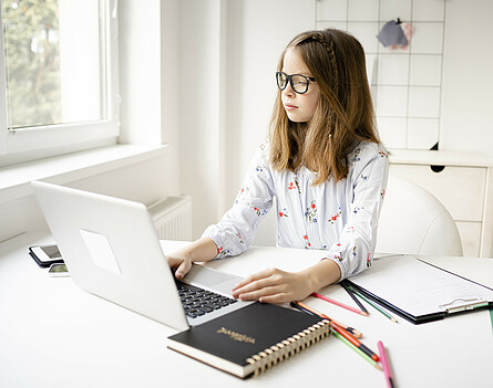 Schülerin sitzt beim Tisch vor dem Laptop