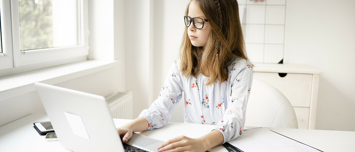 Schülerin sitzt beim Tisch vor dem Laptop