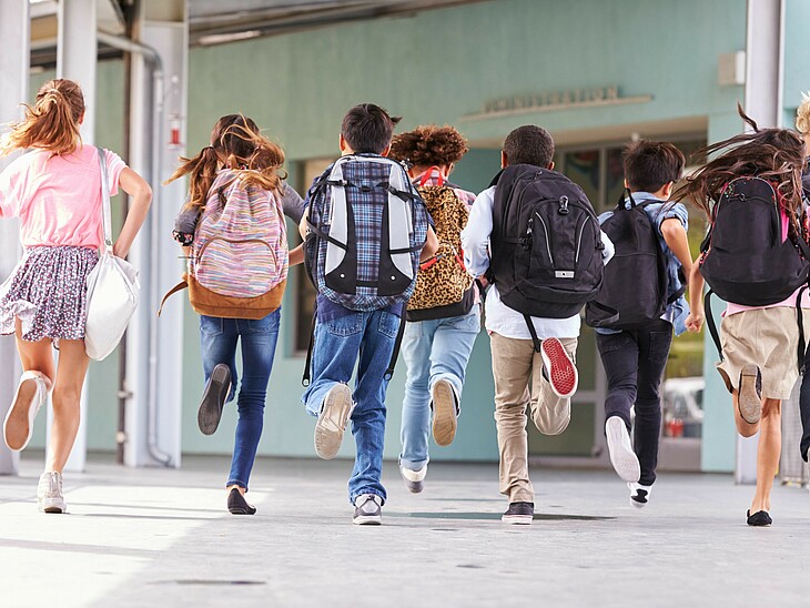 Eine Schülergruppe mit Schultaschen läuft auf das Klassenzimmer zu. Top motiviert von Schulbeginn an. 