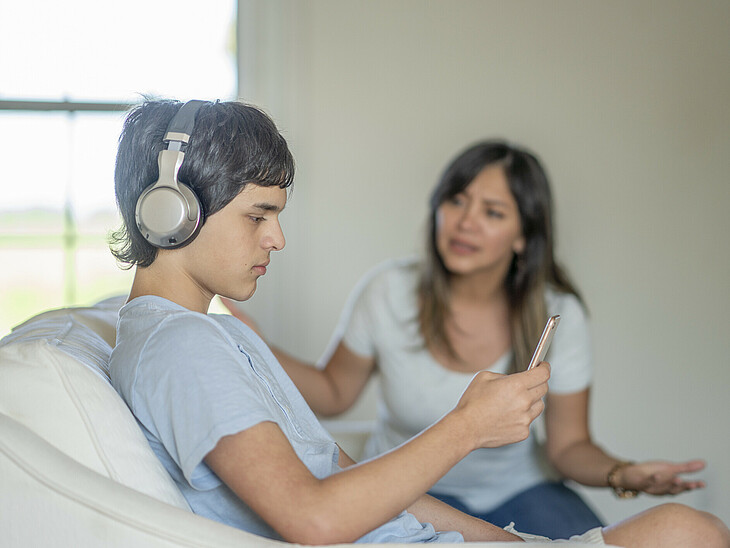 Eine Mutter diskutiert mit ihrem jugendlichen Sohn. Dieser hört dabei Musik und schaut ins Handy.