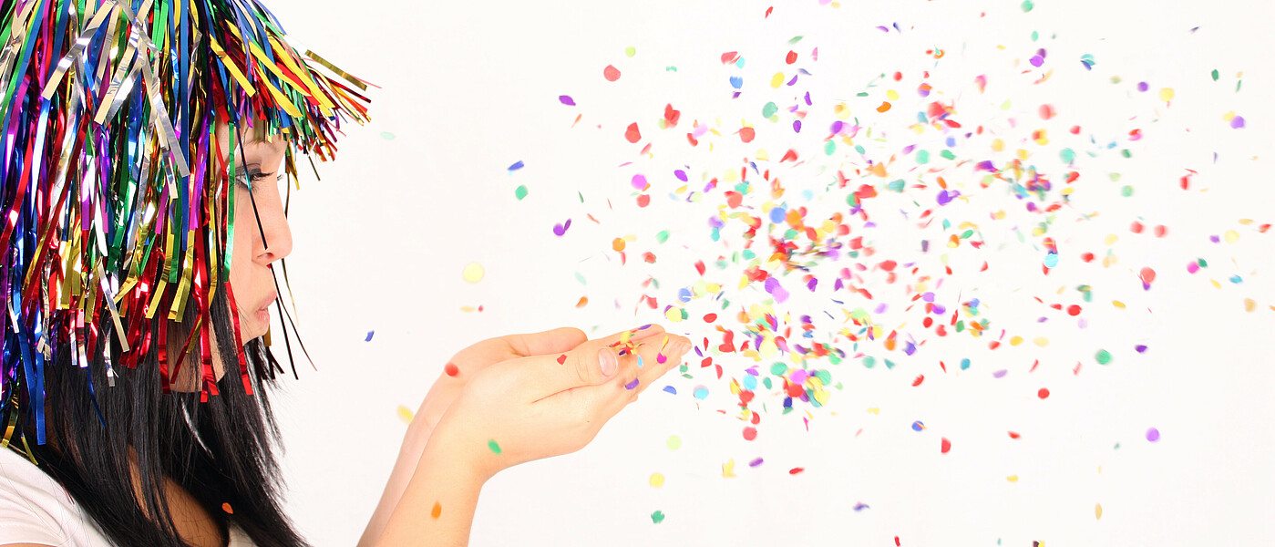 Eine Schülerin mit lustigem Kopfschmuck bläst Konfetti in die Luft