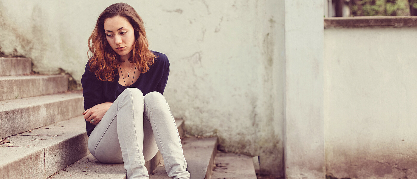Schülerin sitzt demotiviert auf einer Stufe. Sie hat keine Lust auf Schule.