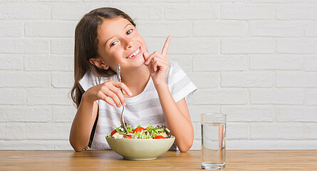 Eine Schülerin sitzt bei Tisch mit einem Glas Wasser und einer Schüssel Salat