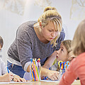 Lehrkraft mit drei Kindern am Tisch sitzend, bei Aufgabenbetreuung.