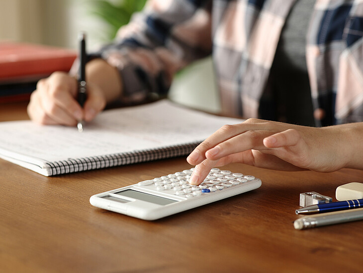 Schüler beim schreiben der Mathe-Schularbeit mit Zettel, Taschenrechner und Schreibgeräte