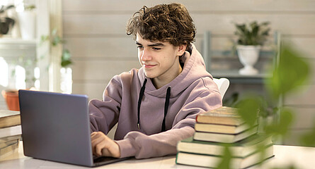 Lächelnder Jugendlicher mit Laptop beim Lernen mit Online Lernplattform