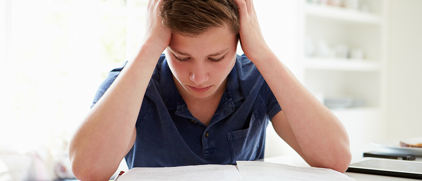 Schüler sitzt beim Tisch mit Kopf in den Händen gestützt und lernt