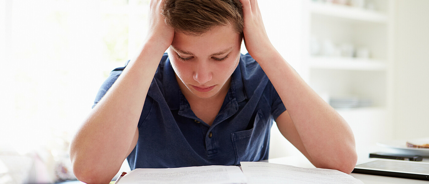 Schüler sitzt beim Tisch mit Kopf in den Händen gestützt und lernt