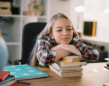 Mädchen lehnt auf Bücherstapel © I-Stock Mädchen sitzt beim Tisch, lehnt sich auf Bücherstapel