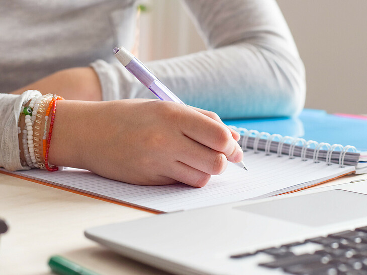 Eine Schülerin schreibt beim Lernen mit der Hand auf einem Schulblock