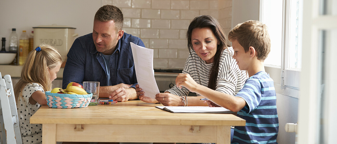 Eltern mit zwei Kindern sitzen beim Tisch und lernen
