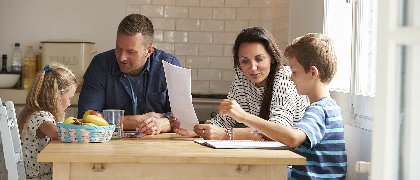 Eltern mit zwei Kindern sitzen beim Tisch und lernen
