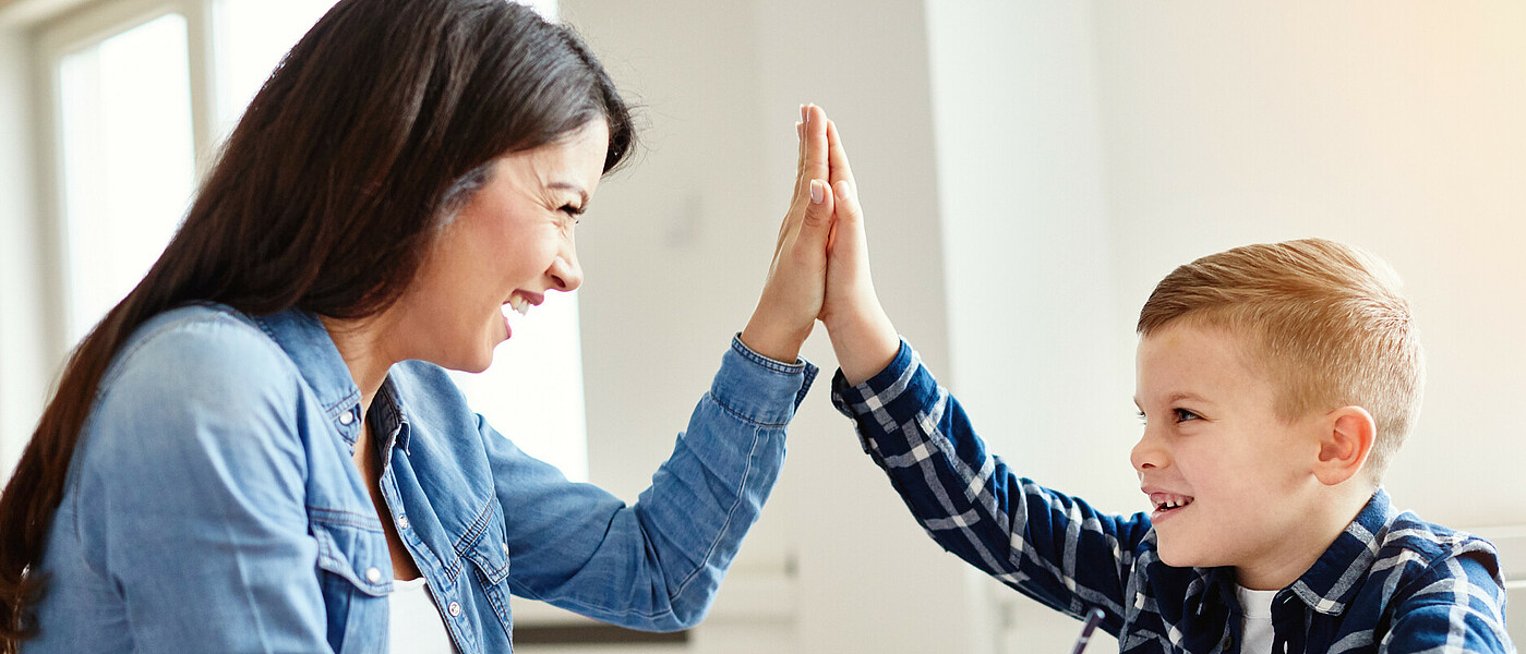 Lehrkraft und ein Kind bei Aufgabenbetreuung, geben einander High Five.