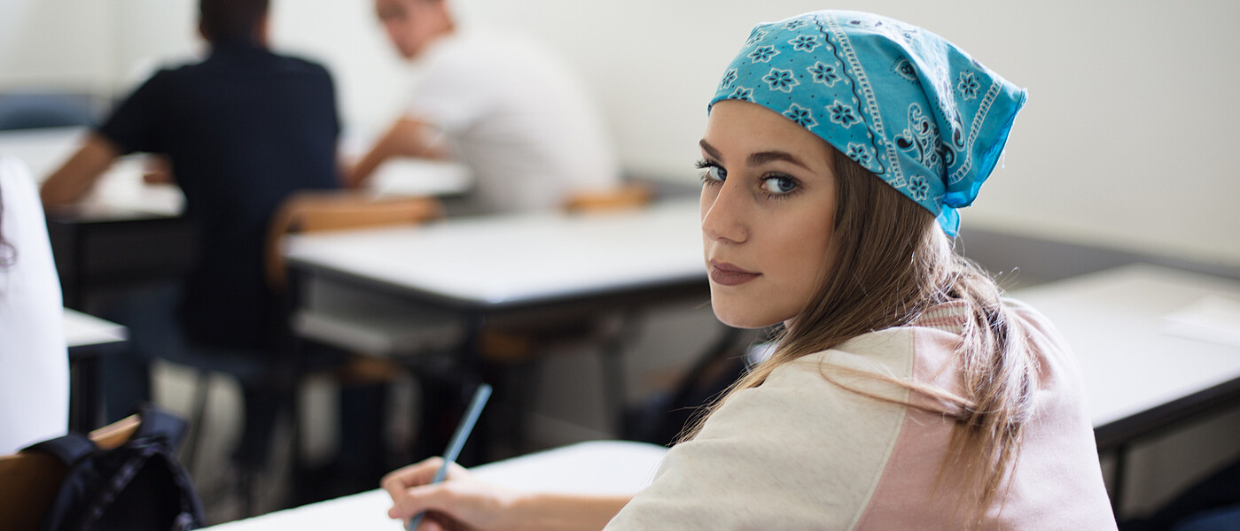 Schülerin beim Schreiben einer Nachprüfung blickt in die Kamera