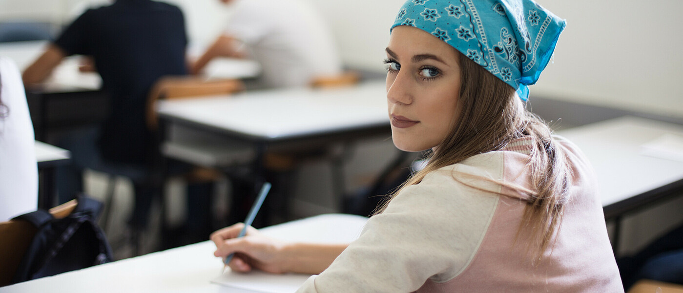 Schülerin beim Schreiben einer Nachprüfung blickt in die Kamera