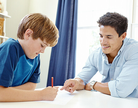 Unterstufenschüler sitzt mit Lehrkraft beim Tisch. Lehrkraft erklärt.