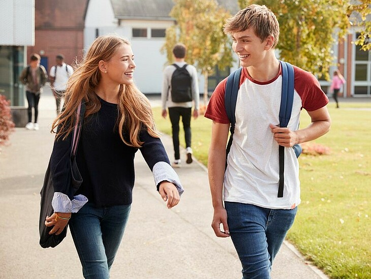 Eine Schülerin und ein Schüler spazieren mit Schulsachen nebeneinander