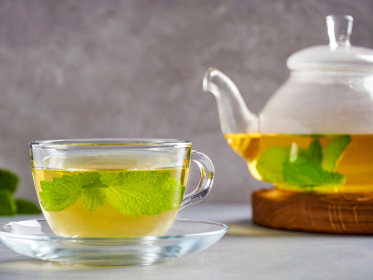 Eine Teetasse gefüllt mit Grüntee neben einer Teekanne
