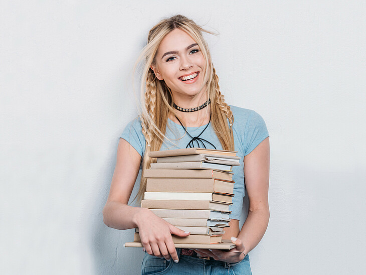 Übersiedlung Eine Schülerin übersiedelt und trägt einen Stapel eingepackter Bücher