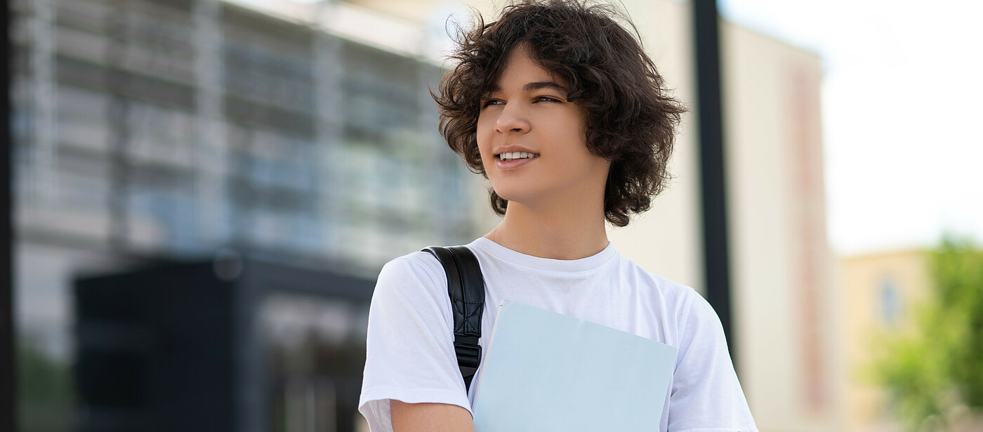 Schüler vor einem Gebäude mit einer Mappe in der Hand