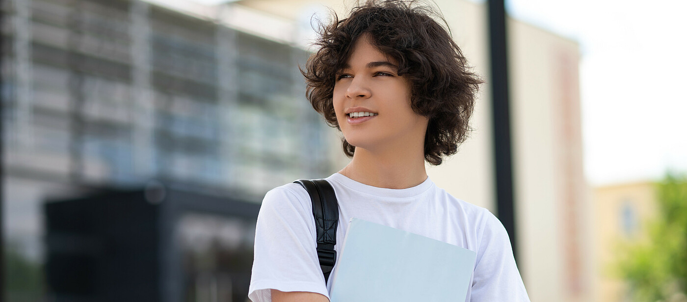 Schüler vor einem Gebäude mit einer Mappe in der Hand