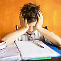 Ein junger Schüler sitzt über den Aufgaben einer schriftlichen Prüfung und stützt verzweifelt seinen Kopf in seine Hände.